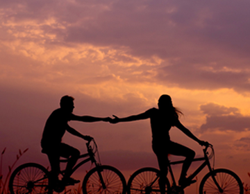 kobieta i mężczyzna jadą na rowerze o wschodzie słońca trzymając się za ręce